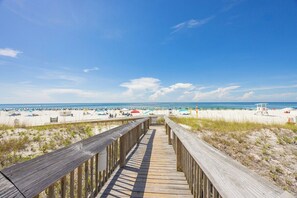A wooden boardwalk leading to a beach with umbrellas and beach chairs.