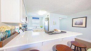Een moderne keuken met een wit aanrecht, barstoelen en een koelkast.