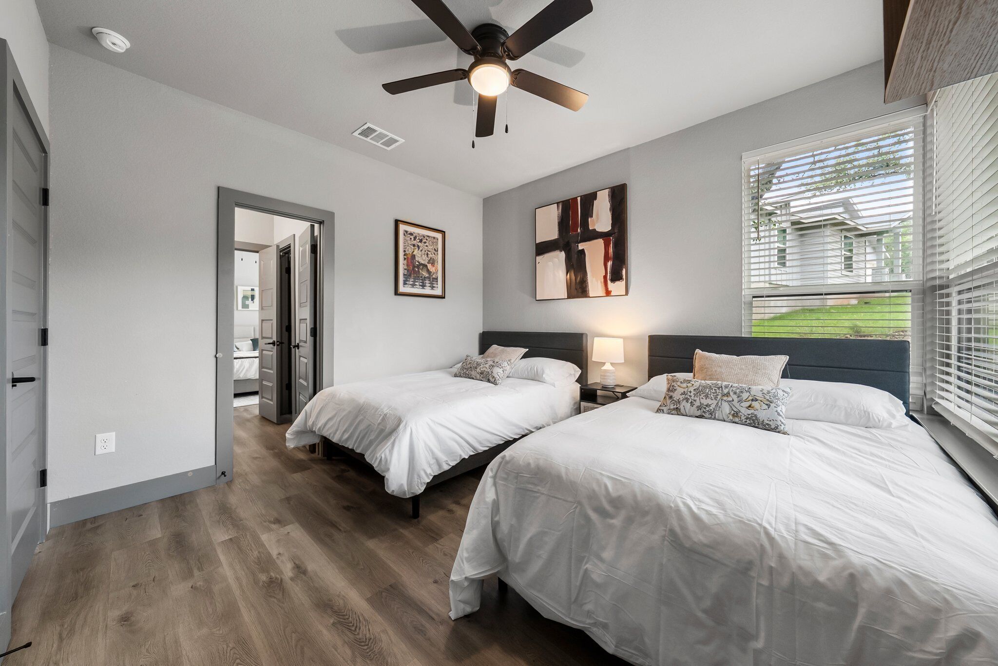 A bedroom with two beds, a ceiling fan, and a window with blinds.