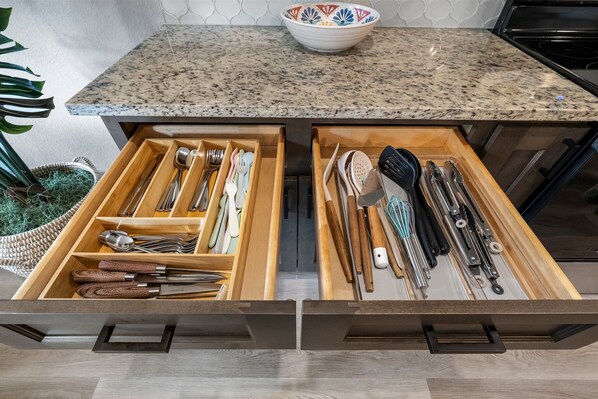 A kitchen with a granite countertop, a bowl, and two drawers with utensils.