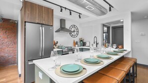 A modern kitchen with a central island, stainless steel appliances, and a brick wall.