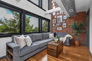 A modern living room with a grey sofa, wooden coffee table, and a brick wall with framed pictures.