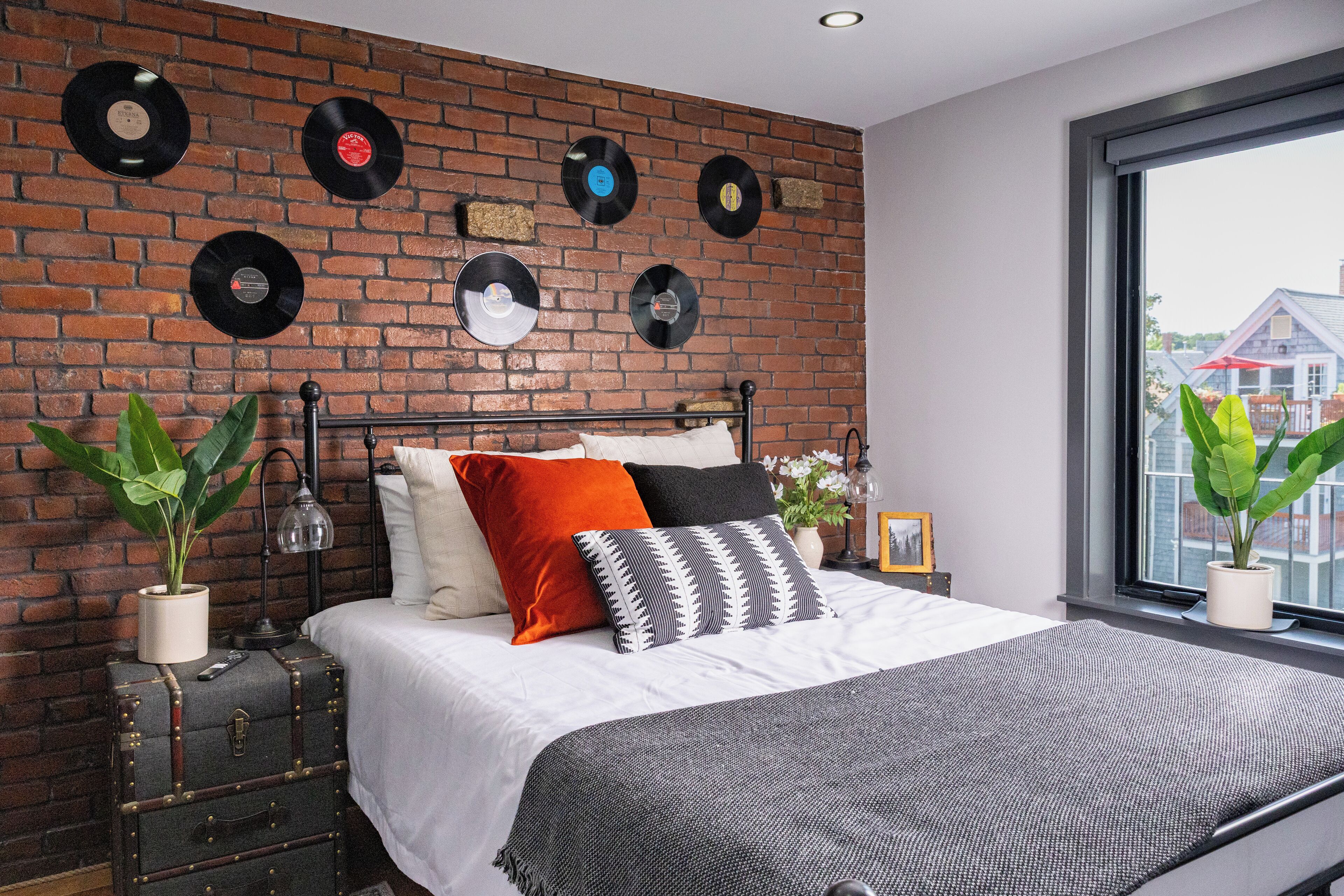 Une chambre avec un mur en briques, un lit avec une literie blanche et une fenêtre donnant sur des immeubles.