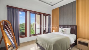 A modern bedroom with a large bed, a wooden nightstand, and a view of greenery through the windows. - Samvara Villa by Kozystay - Ubud (Ubud)