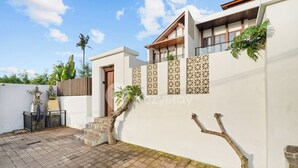 A modern house with a white exterior, a wooden door, and a small staircase leading to a balcony. - Samvara Villa by Kozystay - Ubud (Ubud)