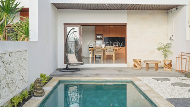 A modern outdoor living area with a pool, seating, and a kitchen visible through an open door. - Samvara Villa by Kozystay - Ubud (Ubud)