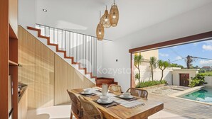 A modern dining area with a wooden table and chairs, a staircase, and a view of a swimming pool. - Samvara Villa by Kozystay - Ubud (Ubud)