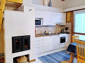 A kitchen with white cabinets, a microwave, a stove, and a window with a view of trees. - Rokua vaulutupa by Interhome (Utajärvi)