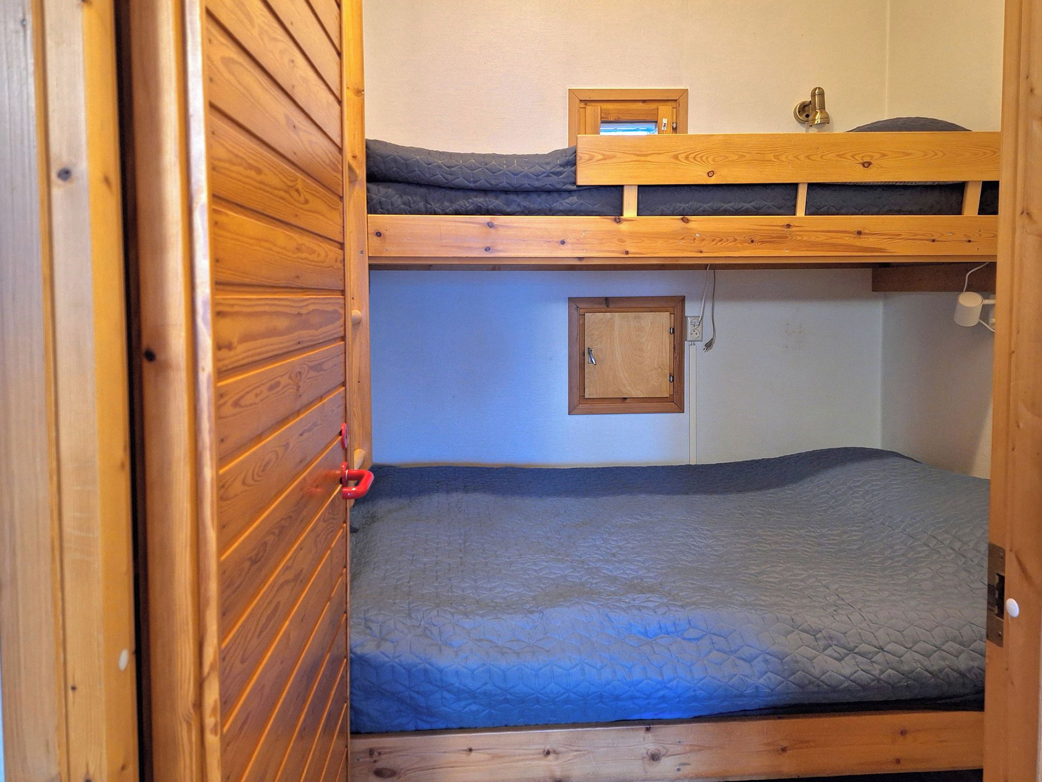 Ein Schlafraum mit Etagenbett, Holzvertäfelung, einem kleinen Schrank und einem roten Türgriff.