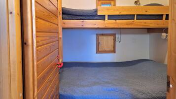 Ein Schlafraum mit Etagenbett, Holzvertäfelung, einem kleinen Schrank und einem roten Türgriff.