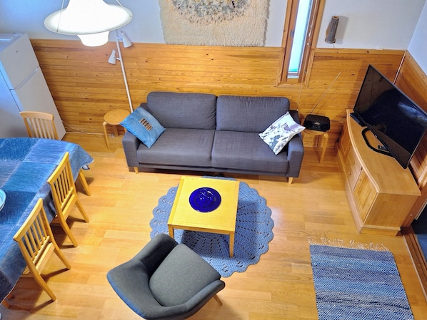 A cozy living room with a sofa, a small table, a chair, a television, and a radio.