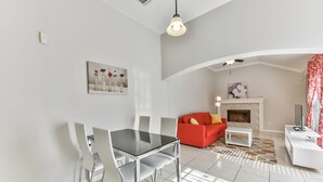 Una sala de estar moderna con chimenea, un comedor con una mesa y sillas de vidrio, y un sofá rojo.