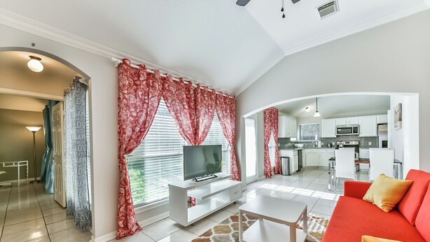 Una sala de estar moderna con televisión, sofá y cocina al fondo.