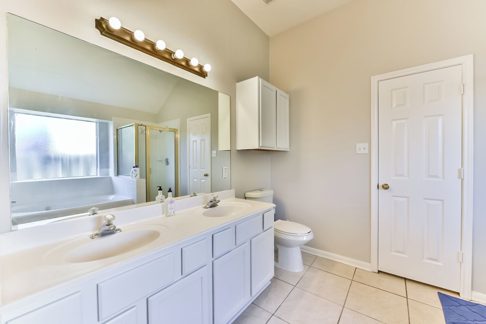 A bathroom with a large mirror, two sinks, a toilet, and a shower enclosure.