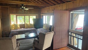 A cozy cabin room with a bed, a desk, a chair, a television, and large windows.