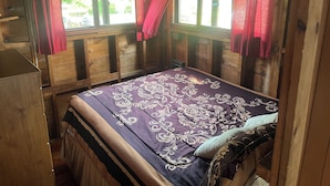 A wooden cabin room with a bed, a small table, and a window with red curtains.