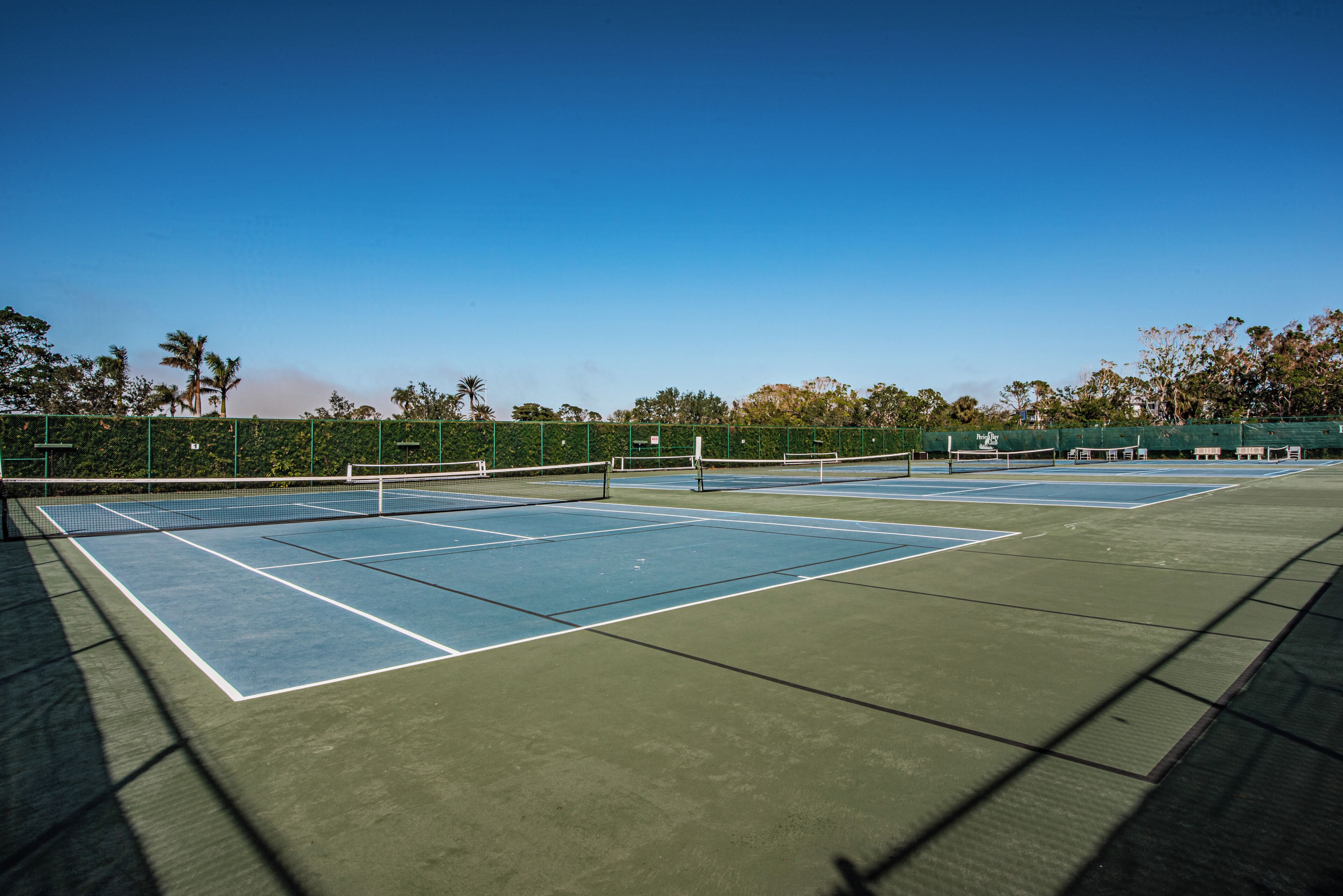En tennisbane med net, omkranset af et hegn og træer.