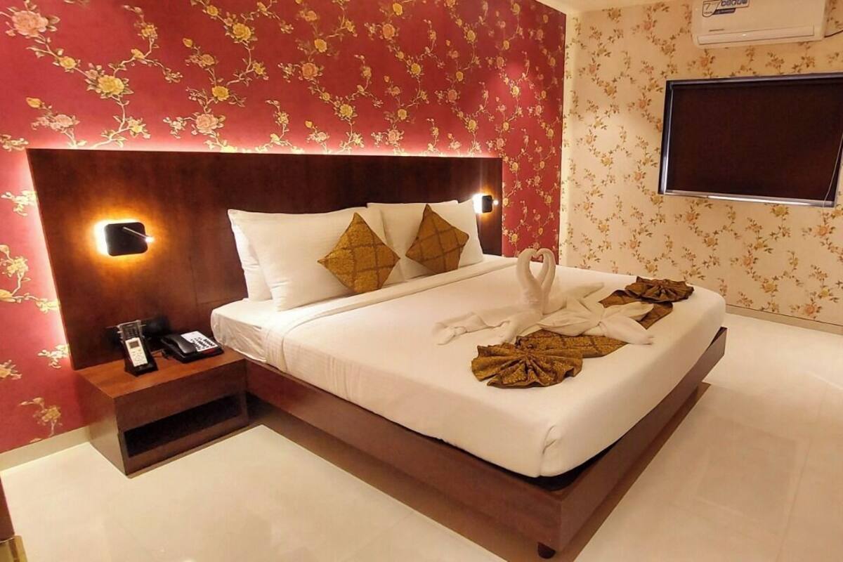 Habitación de hotel con cama, mesita de noche con teléfono, televisor montado en la pared y papel tapiz floral.