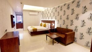 A hotel room with a bed, a sofa, a desk, and a mirror. - Hotel madhuban  (Silvassa)