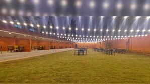 An indoor venue with rows of tables and chairs, a grassy area in the center, and a ceiling with numerous lights. - Hotel madhuban  (Silvassa)