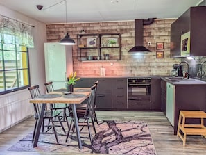 Une cuisine moderne avec un mur de briques en guise de crédence, un four encastré et un coin repas comprenant une table et des chaises.