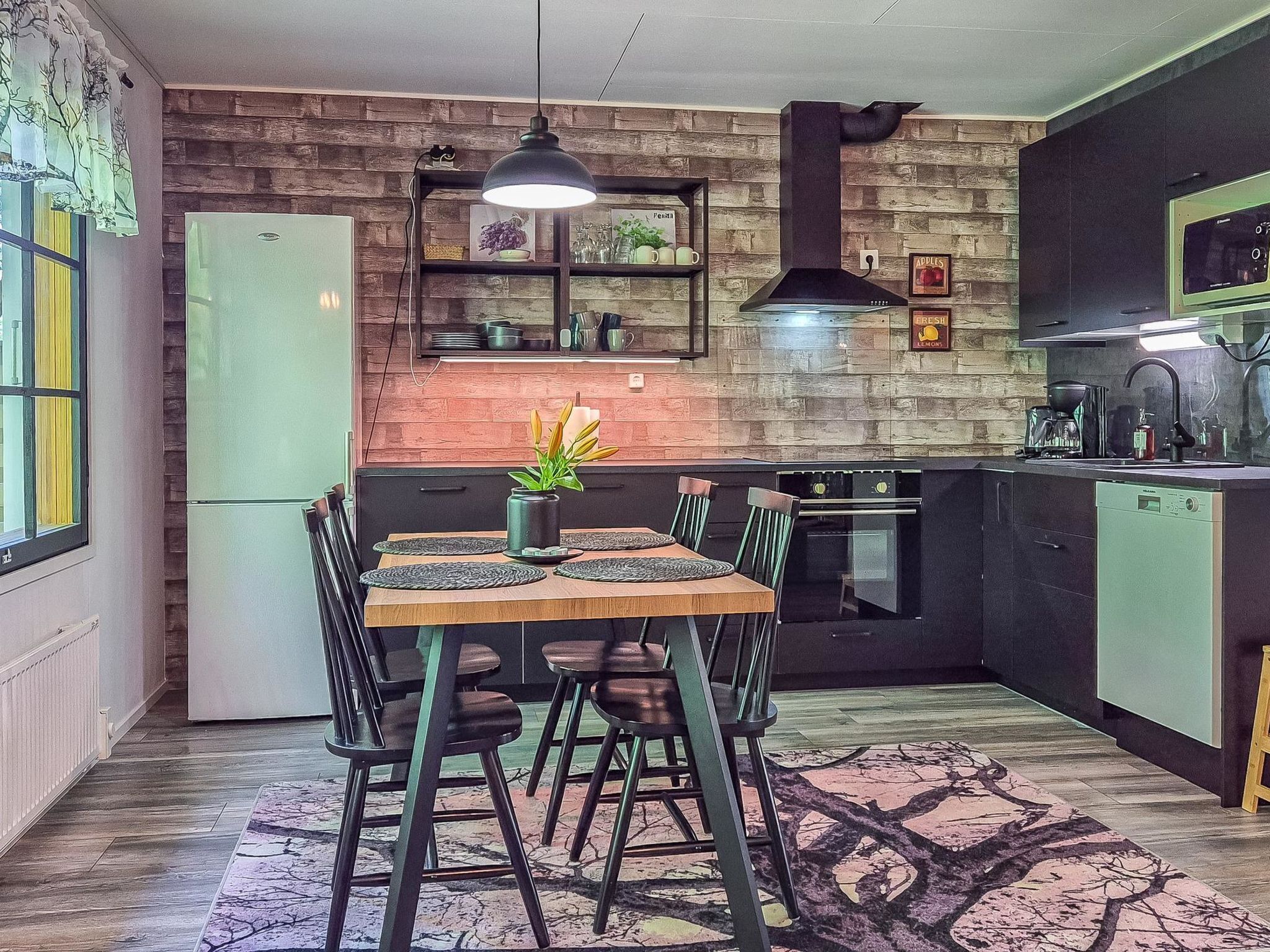 Une cuisine moderne avec un mur de briques derrière l’évier, un four encastré et un coin repas comprenant une table et des chaises en bois.