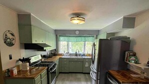 Una cocina con armarios verdes, una estufa, un refrigerador y una ventana con vistas al exterior.