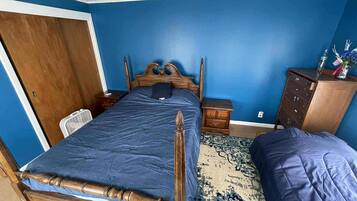 Un dormitorio con una cama de madera, una pared azul, un aparador de madera y una alfombra estampada.