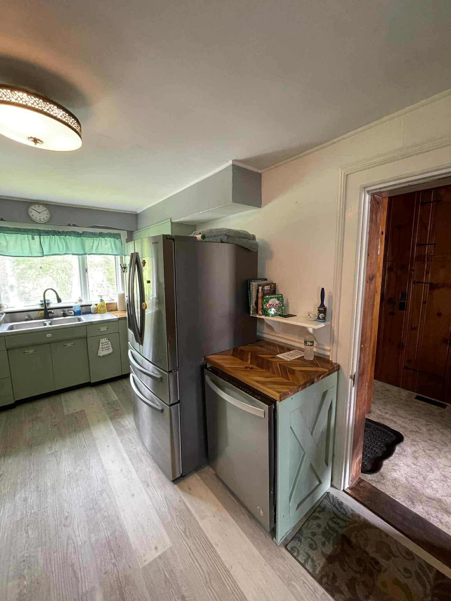 A compact kitchen with a refrigerator, a dishwasher, and a wooden countertop.