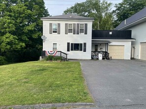 Une maison à deux étages avec un garage, un porche à l’avant et un petit jardin devant.