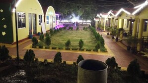A courtyard with a central lawn, surrounded by yellow buildings with arched doorways, and potted plants along the pathways. - Nature4 Resort   (Purulia)