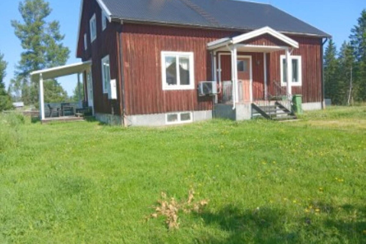 A red wooden house with a porch, a chimney, and a grassy yard.