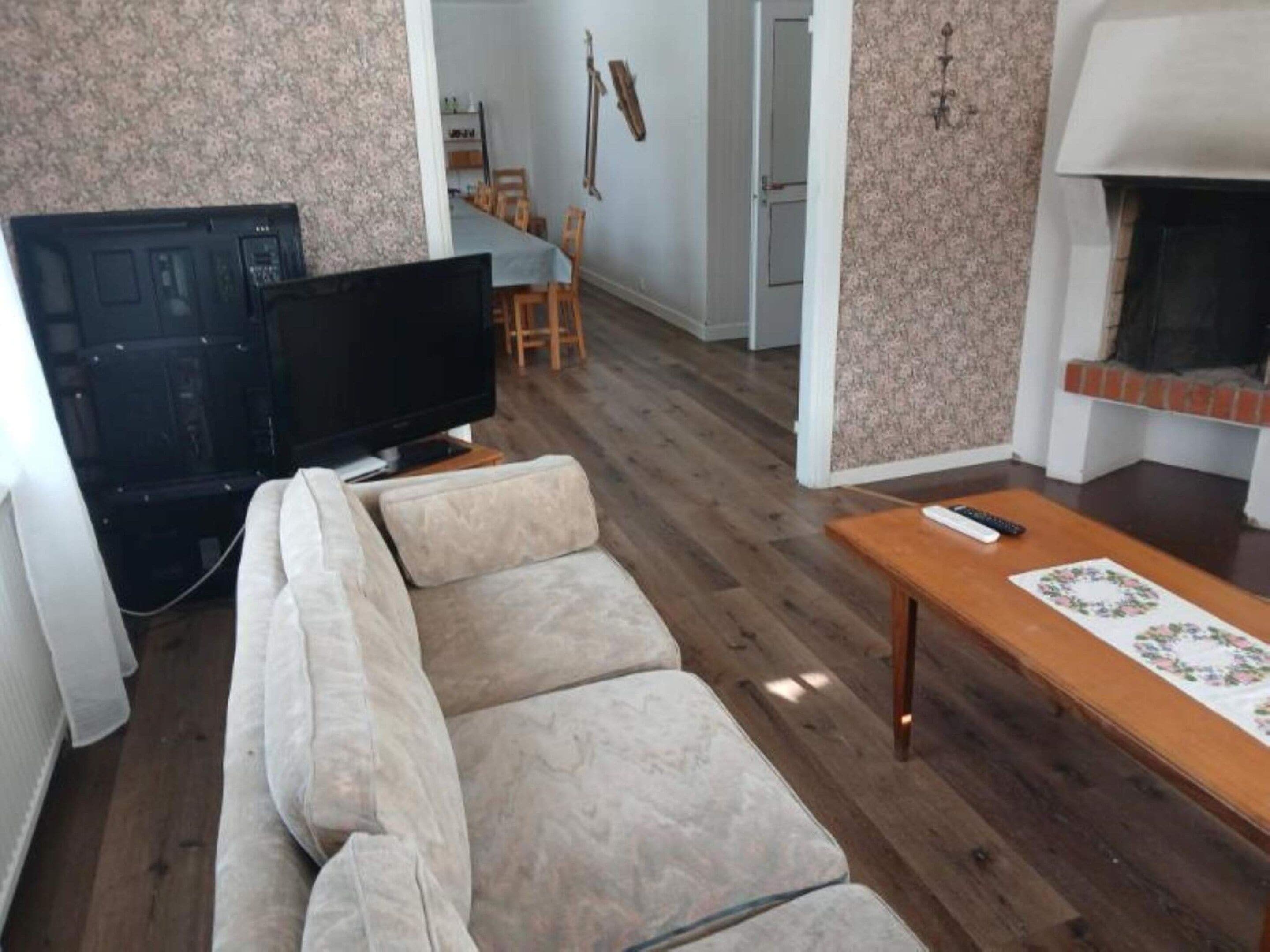 A living room with a sofa, a television, a fireplace, and a dining area in the background.