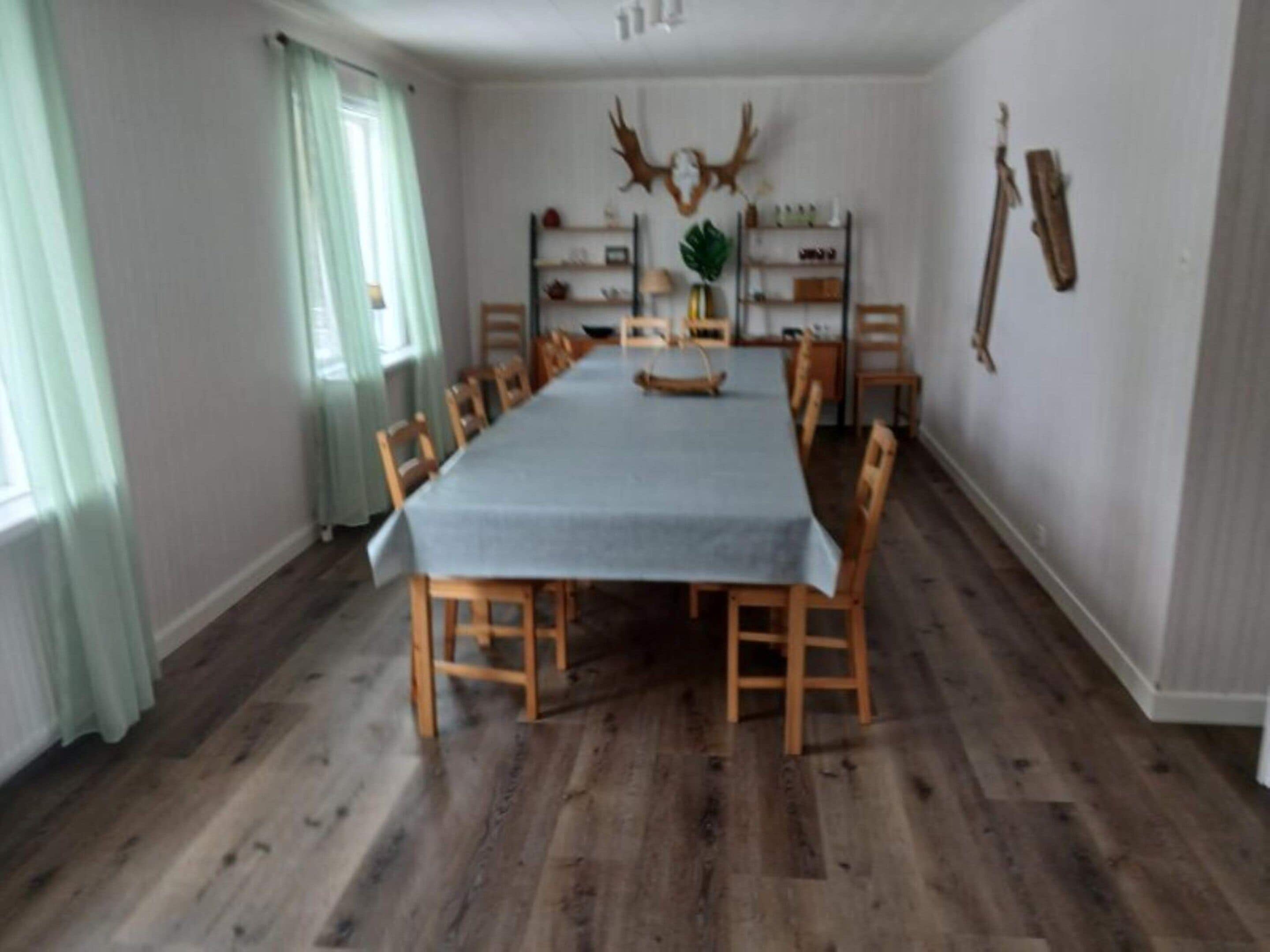 Una sala de dinar amb una taula llarga, cadires de fusta i un sòl de fusta rústic.