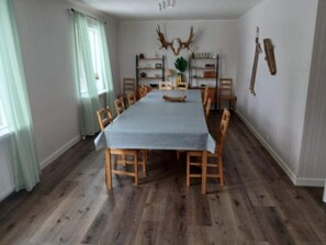 A dining room with a long table, wooden chairs, and a rustic wooden floor.