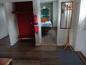 Una habitación con una cama, un perchero rojo, un extintor y suelo de madera.
