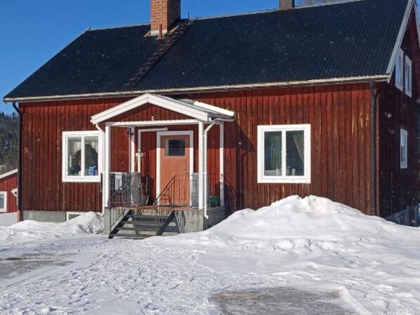 A red wooden building with a black roof, a front porch, and a chimney.