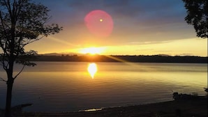 Un atardecer sobre un lago tranquilo, con un árbol a la izquierda y un cielo despejado.