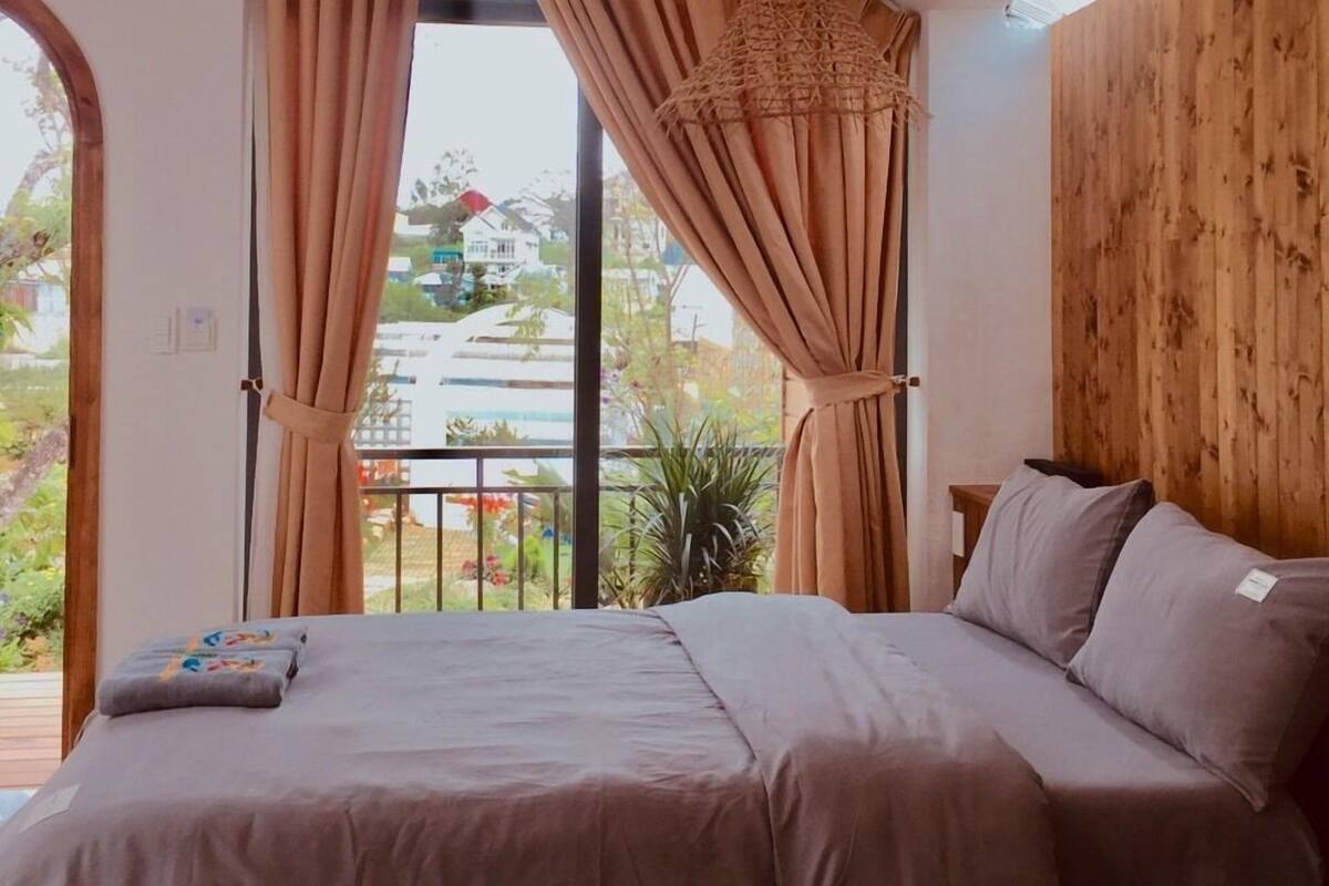 A bedroom with two beds, large windows with curtains, a wooden wall, and a hanging light fixture.