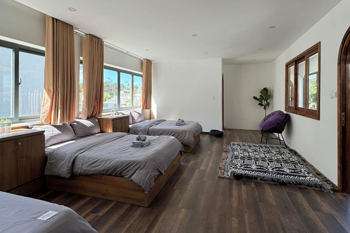 A modern bedroom with two beds, a large window, and a wooden floor.