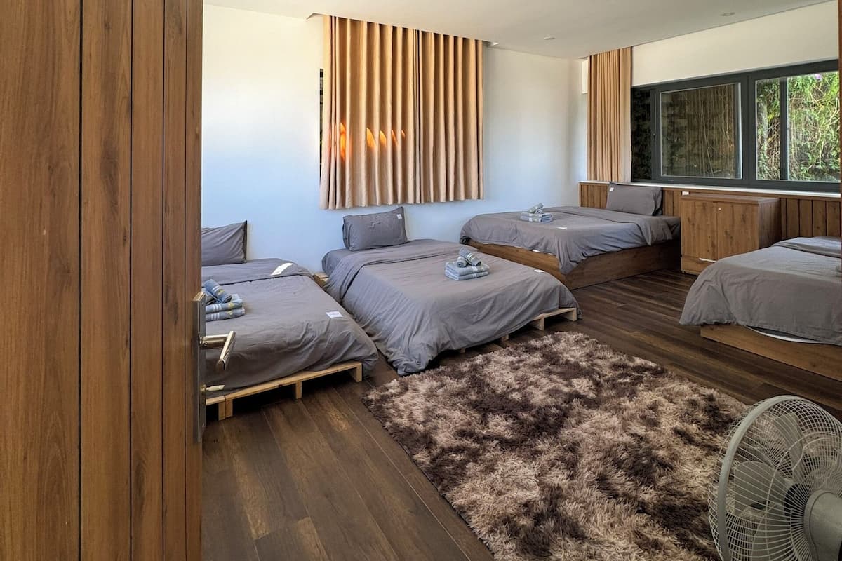 A modern bedroom with a large bed, two smaller beds, a wooden floor, a fluffy rug, and a ceiling fan.