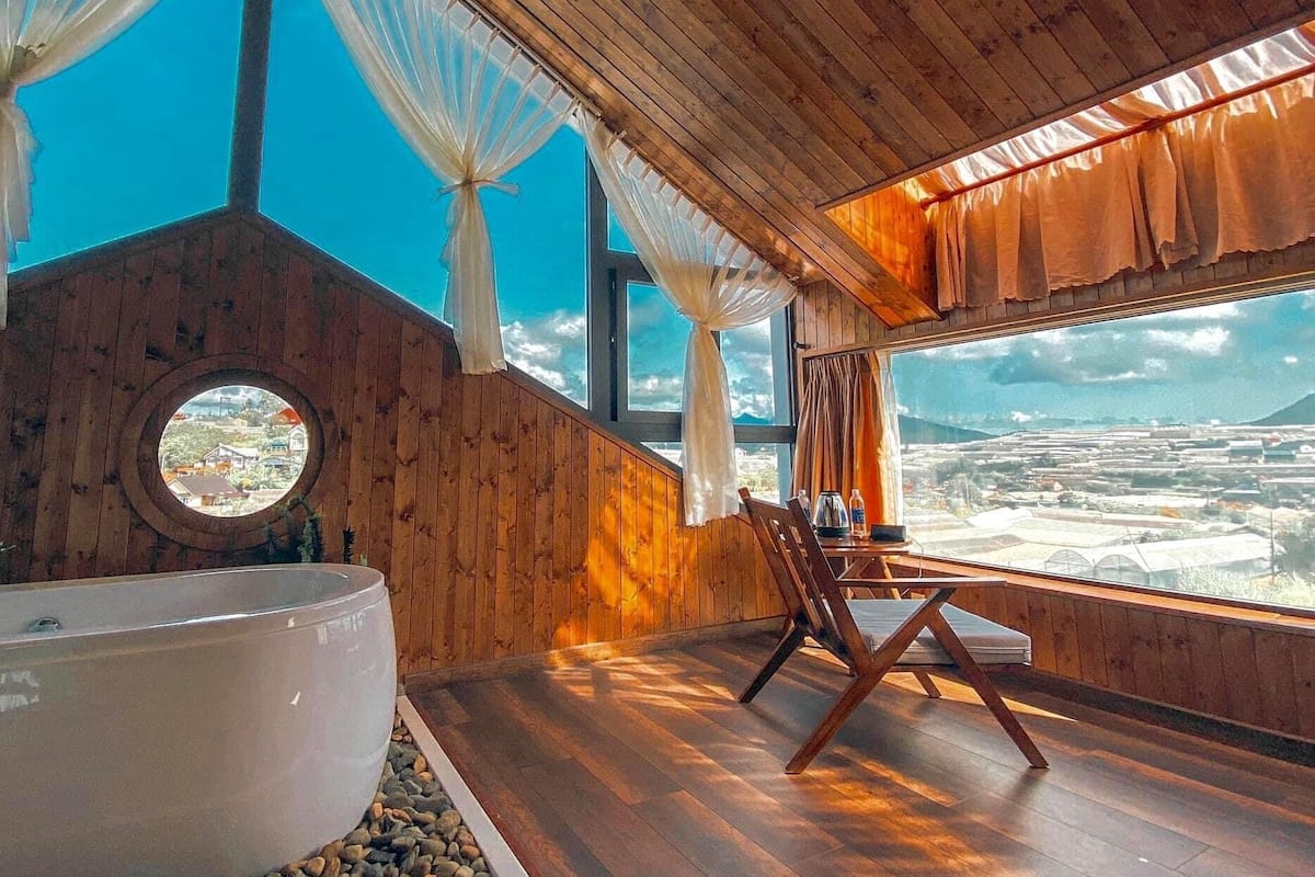 A room with a large bathtub, wooden walls, and a view of a landscape through large windows.