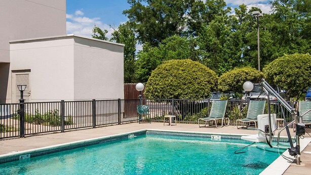 A clear swimming pool with a metal ladder, lounge chairs, and a fence. - Travelodge by Wyndham Flowood (Flowood)