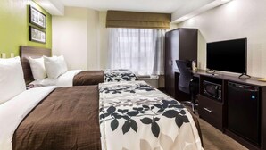 A hotel room with two beds, a desk with a television, a microwave, and a refrigerator. - Travelodge by Wyndham Flowood (Flowood)