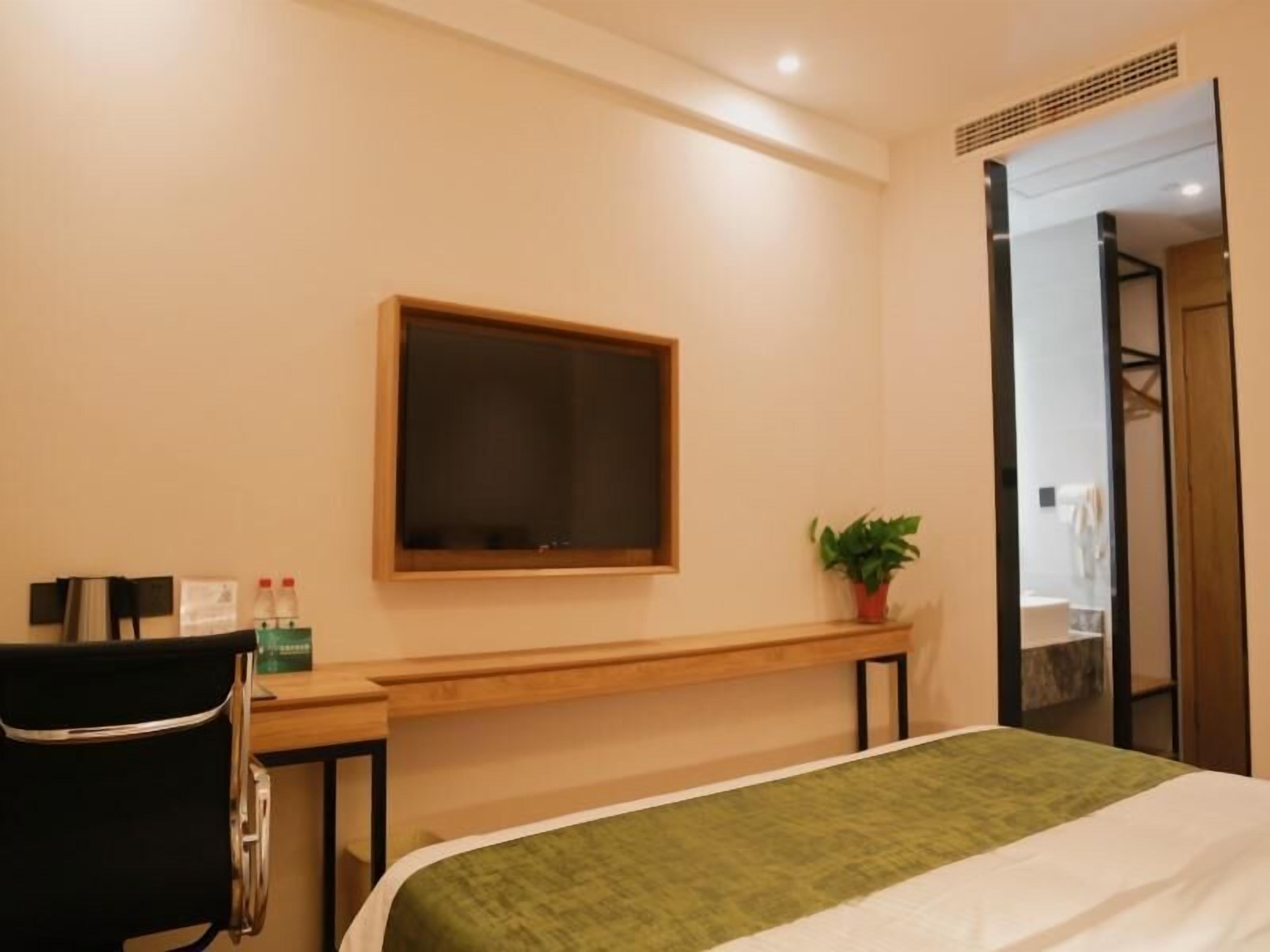 Quarto de hotel com cama, escrivaninha, cadeira, planta em vaso e espelho.