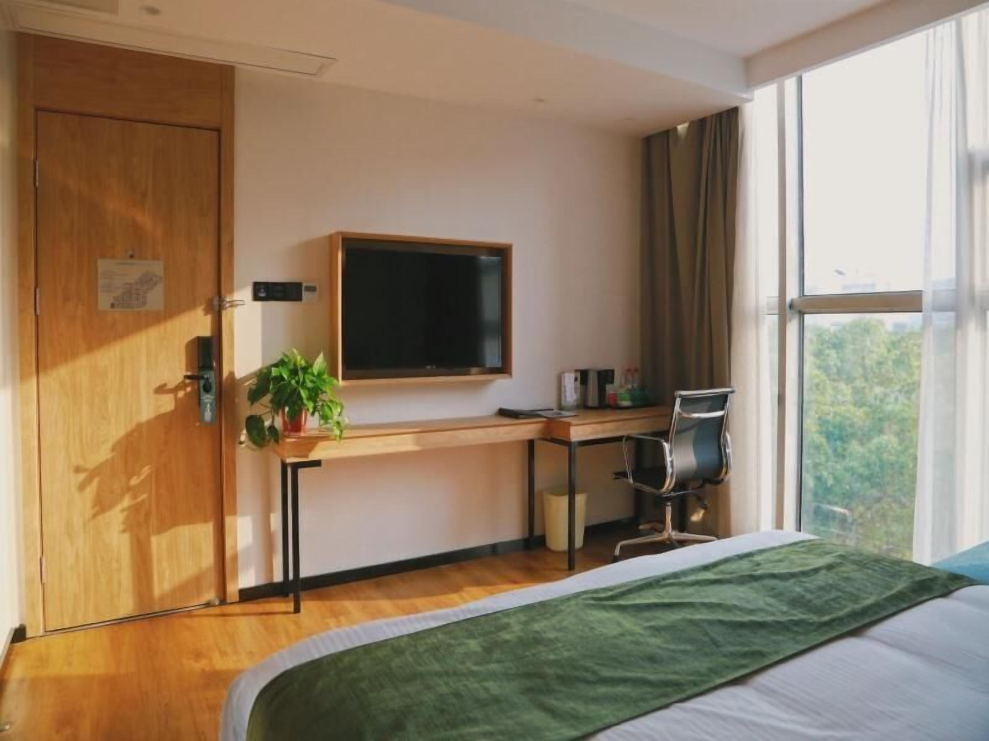 A hotel room with a bed, a desk, a chair, a TV, and a window with a view.
