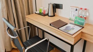 A hotel room with a wooden desk, a black office chair, a laptop, a kettle, a coffee maker, and a small table with bottles and a brochure. - Greentree Inn Nanjing Baijiahu Express Hotel (Nanjing)