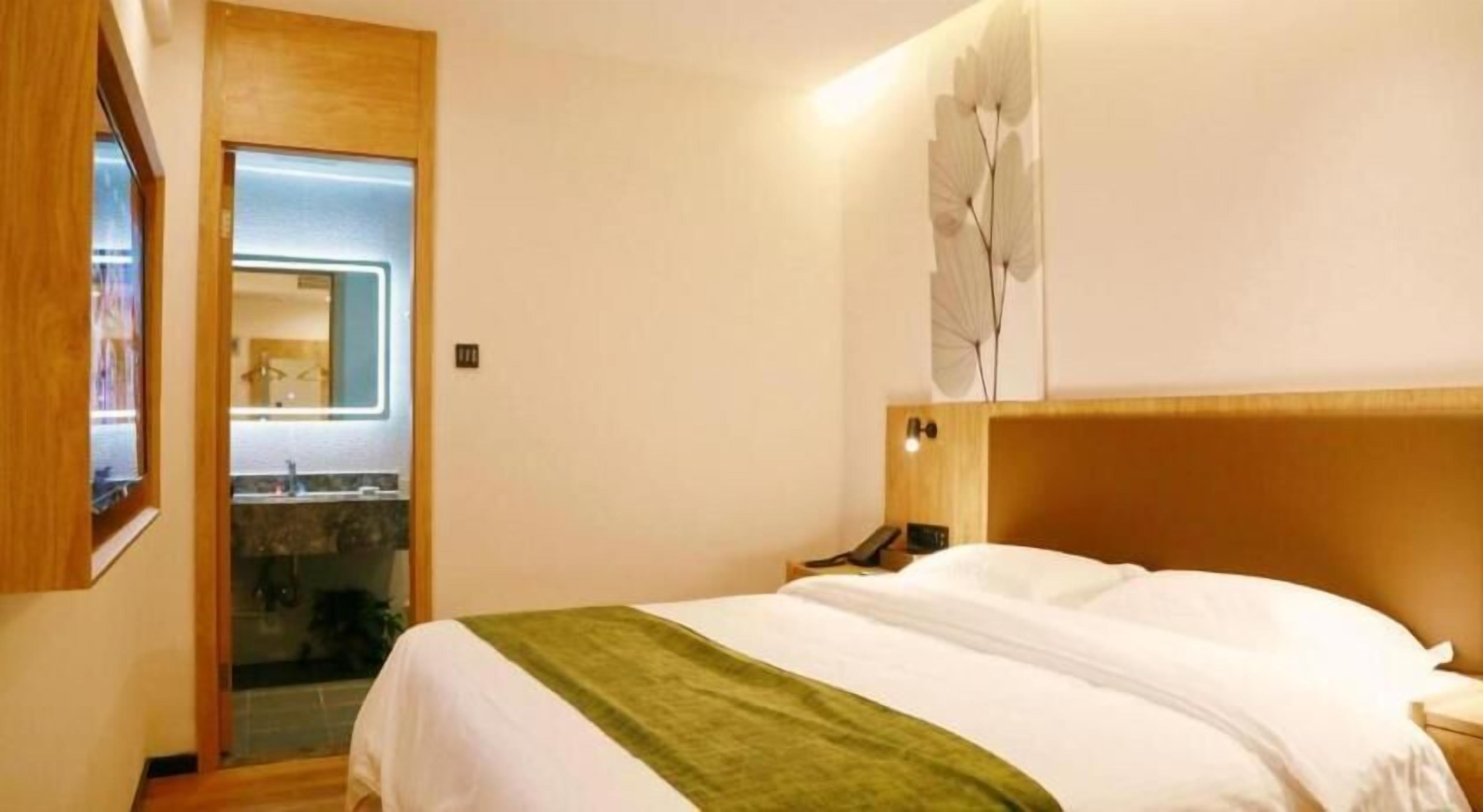 A hotel room with a bed, a nightstand, a mirror, and a bathroom visible through an open door.