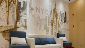 A hotel lobby with a large wall mural of NYC landmarks, a white sofa, and two armchairs. - Greentree Inn Nanjing Baijiahu Express Hotel (Nanjing)