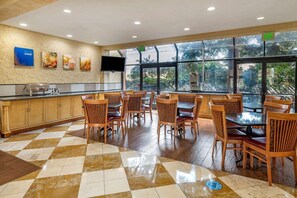 A dining area with wooden chairs and tables, a buffet counter, and a large window with a view of trees.